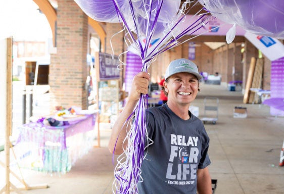 person wearing a baseball hat holding purple balloons at a Relay for Life event